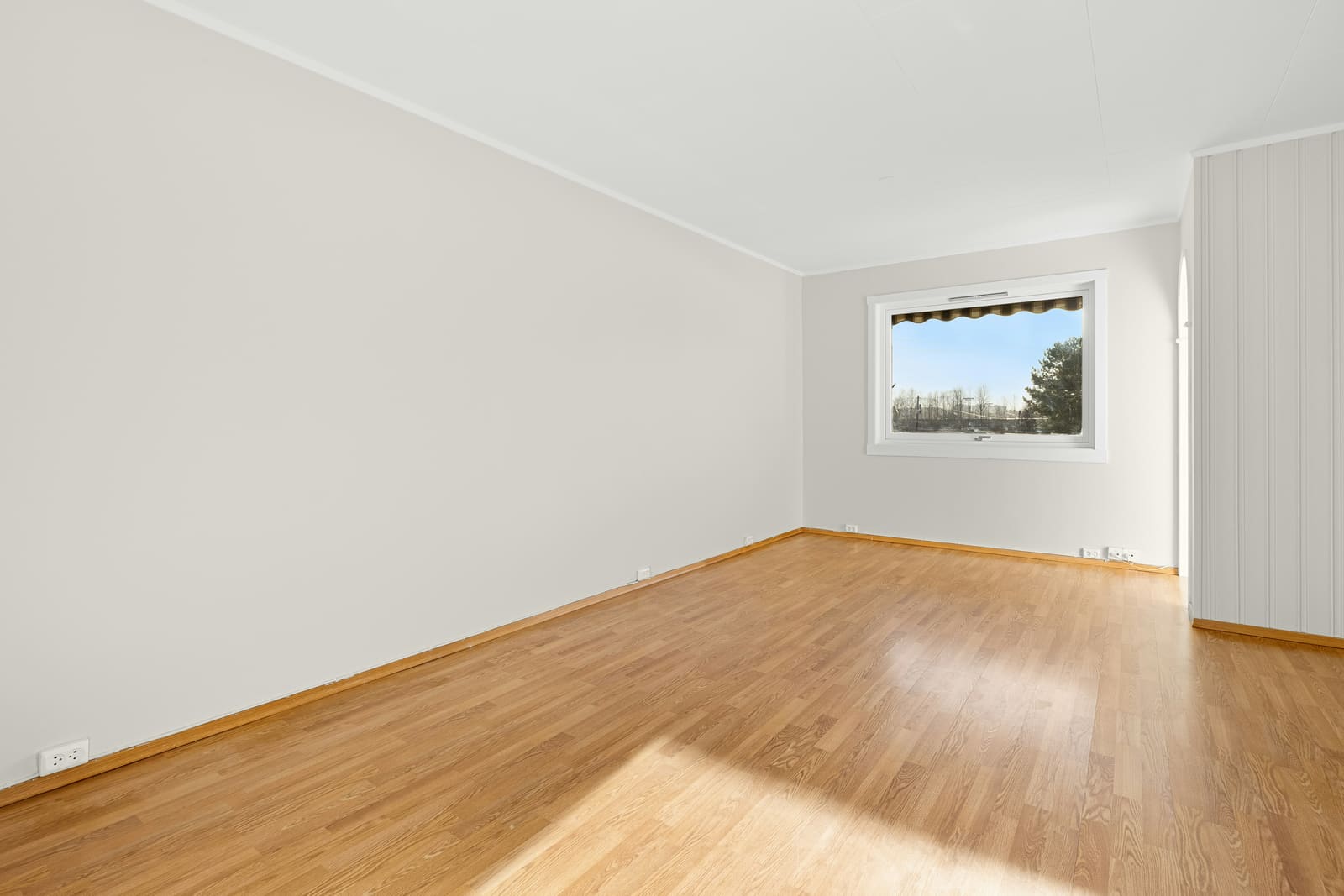 Foto original de uma sala de estar vazia, com piso de madeira e janela ao fundo